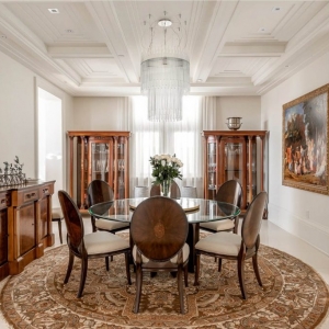 Simple dining room with a beautiful coffered ceiling. White beams and coffers with a crystal chandelier. Round glass table with wood chairs.
