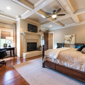 Master bedroom coffered ceiling with white beams and tan coffers. Gas fireplace with tile and wood surround.