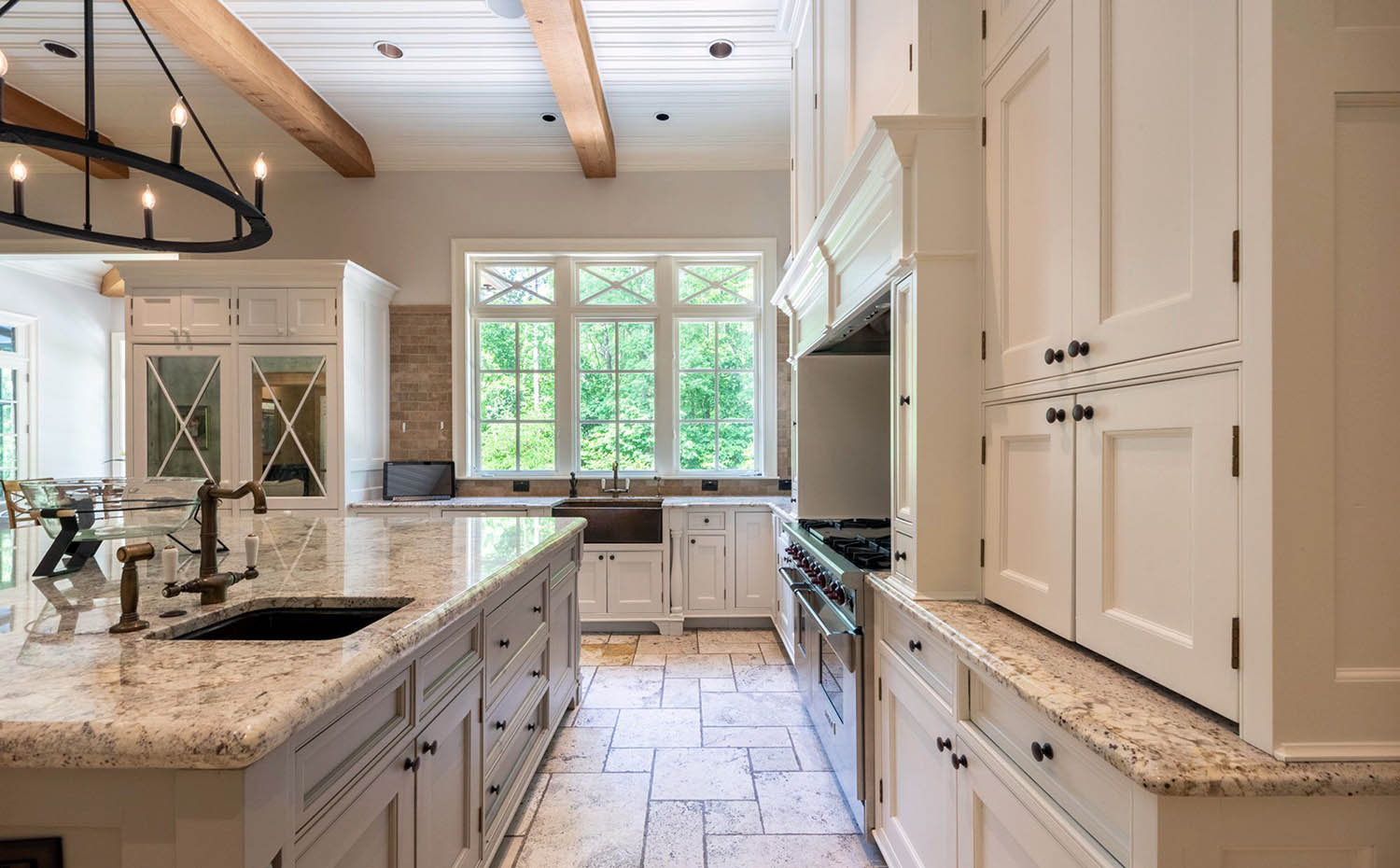 Beautiful cream colored kitchen cabinets with real wood ceiling beams, granite countertops and stone tile backsplash. Black knobs.