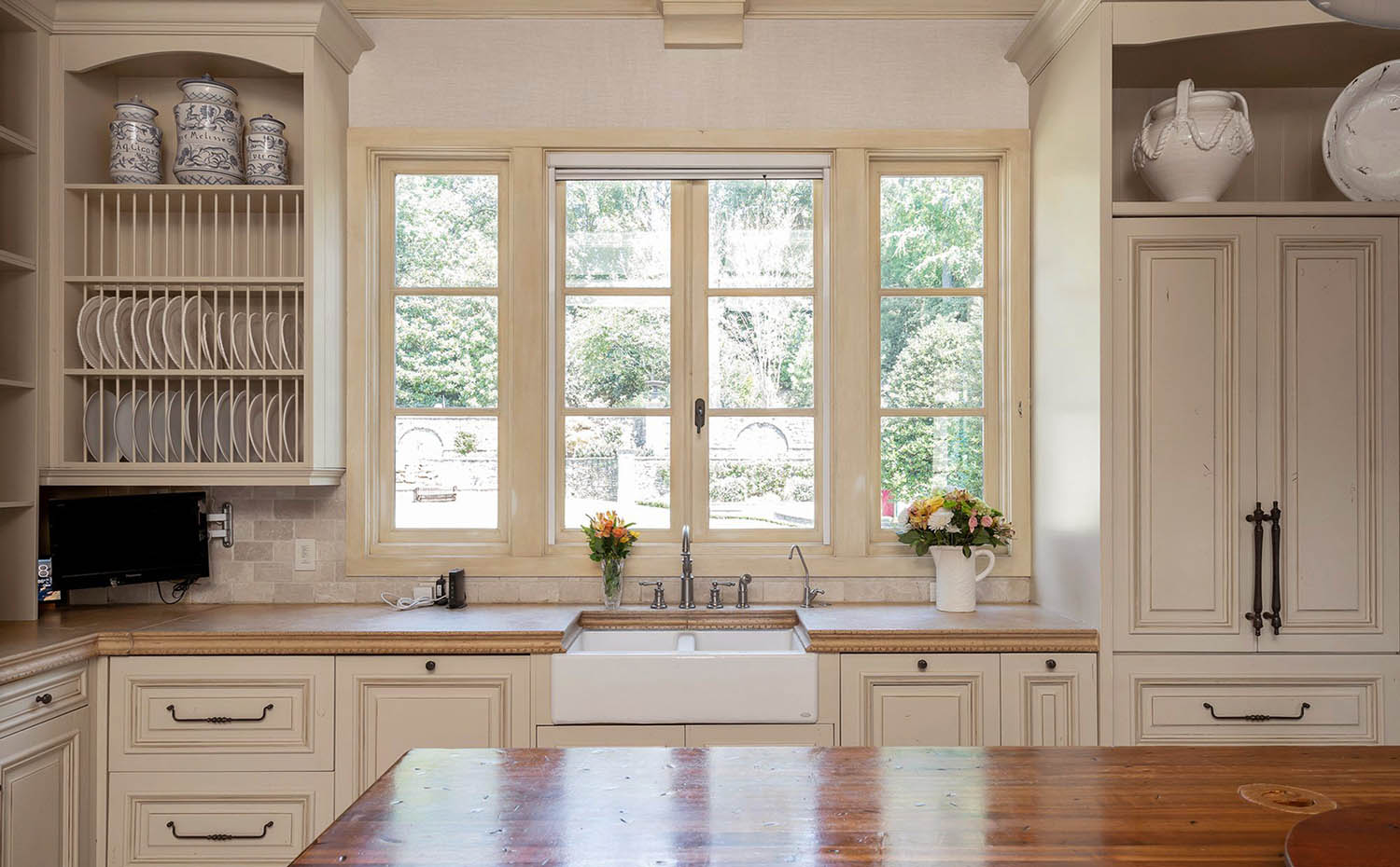 Beautiful cream colored kitchen cabinets with stone backsplash and butcher block countertops. Black hardware. Matching cream trim.