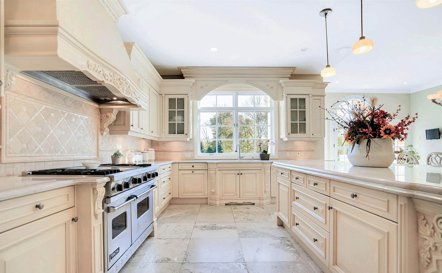 Fantastic luxury kitchen featuring cream colored cabinets and matching stone floors and backsplash. Marble countertops with veins of warm gray.