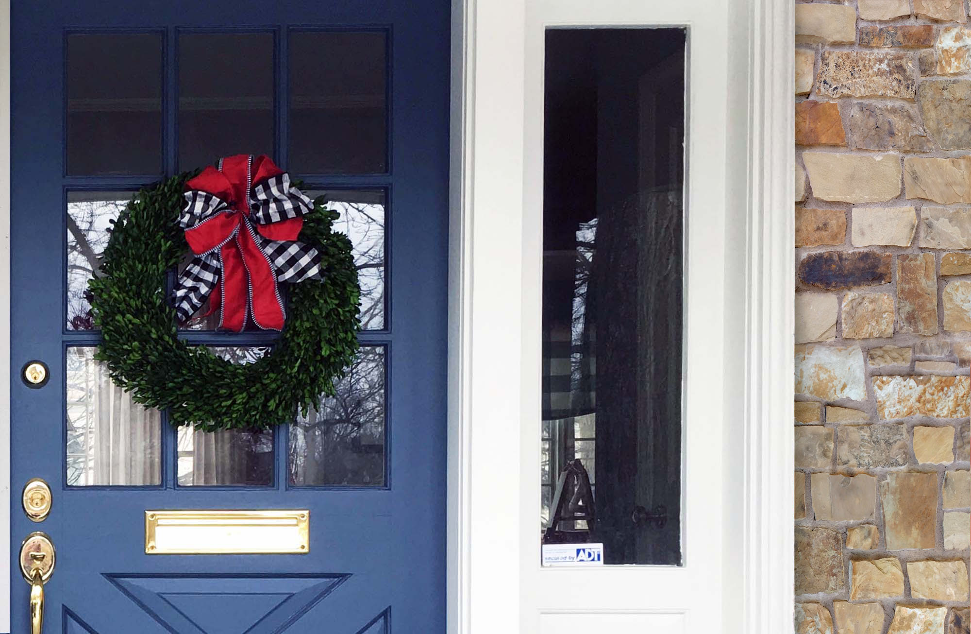royal blue front door with gold hardware, white trim, sidelights, earth toned stone veneer, wreath hung on the door