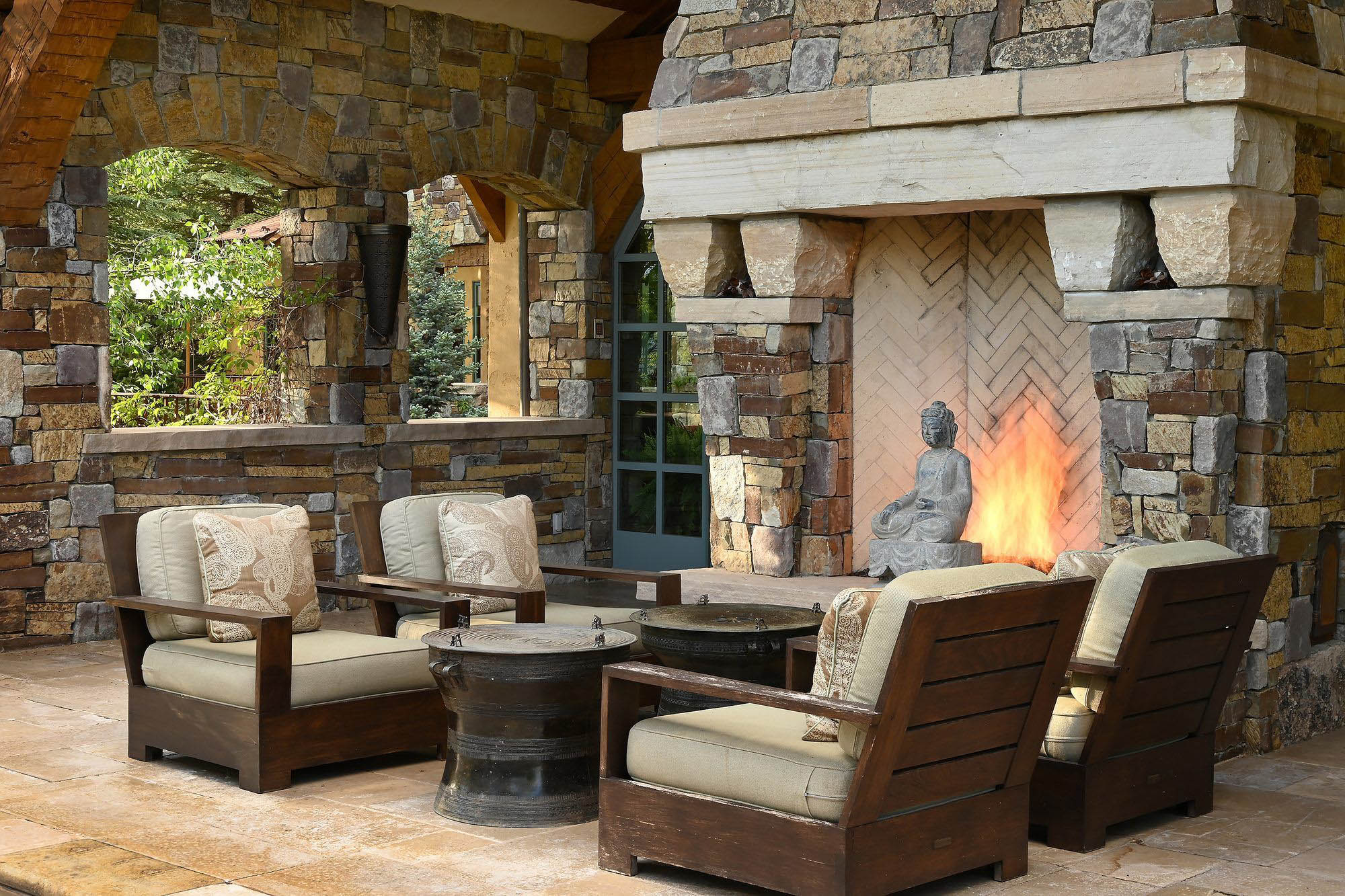 Rustic outdoor patio furniture set. Real wood chairs with tan cushions and throw pillows. Beautiful outdoor patio fireplace with lots of stone veneer.
