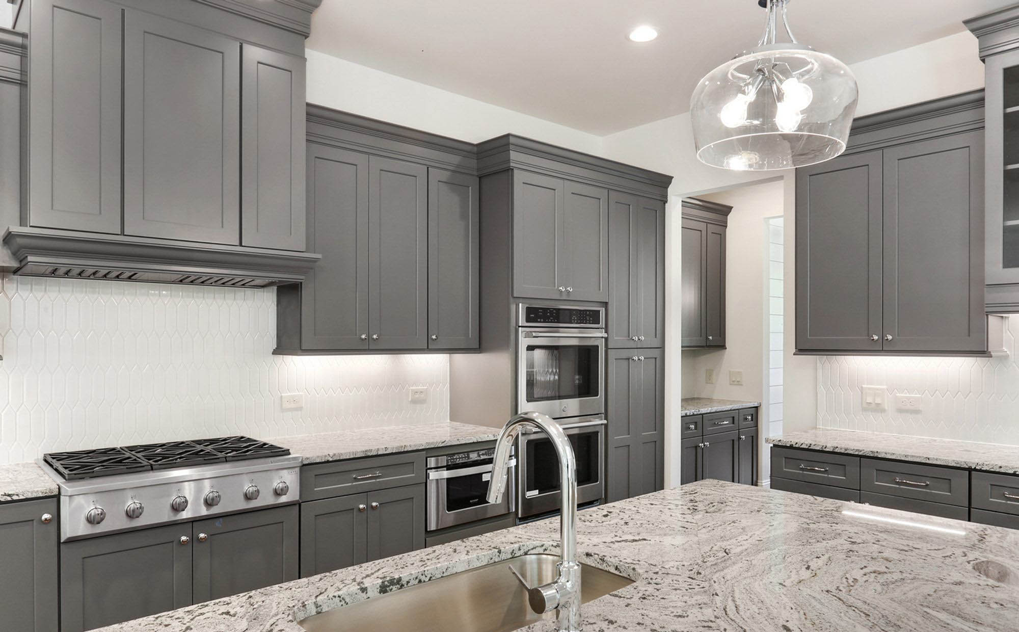 White and gray granite countertops with gray shaker style cabinets and white backsplash.