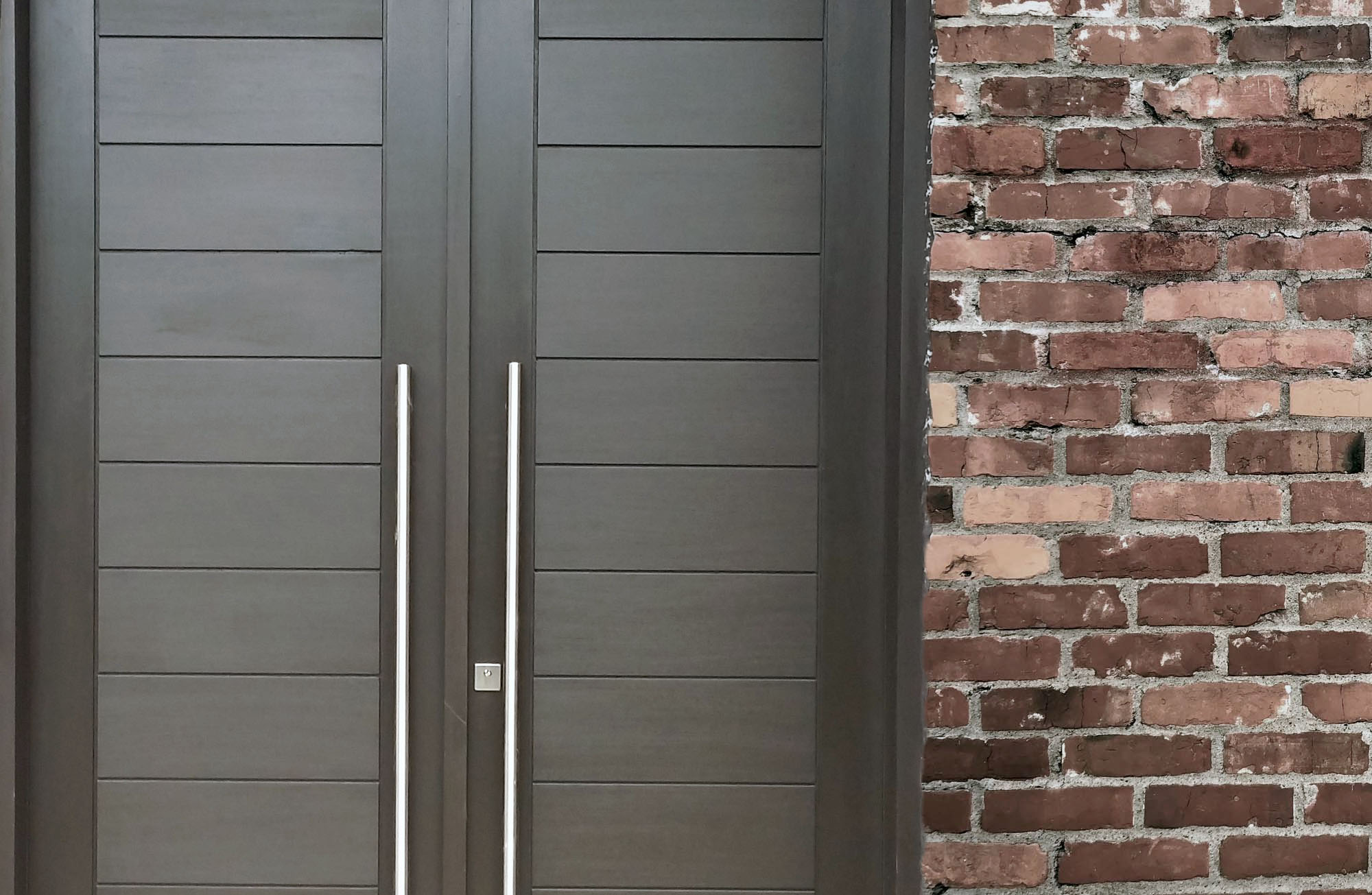 Modern dark gray french style front door with stainless steel pole handles and square dead bolt on a red brick house. 