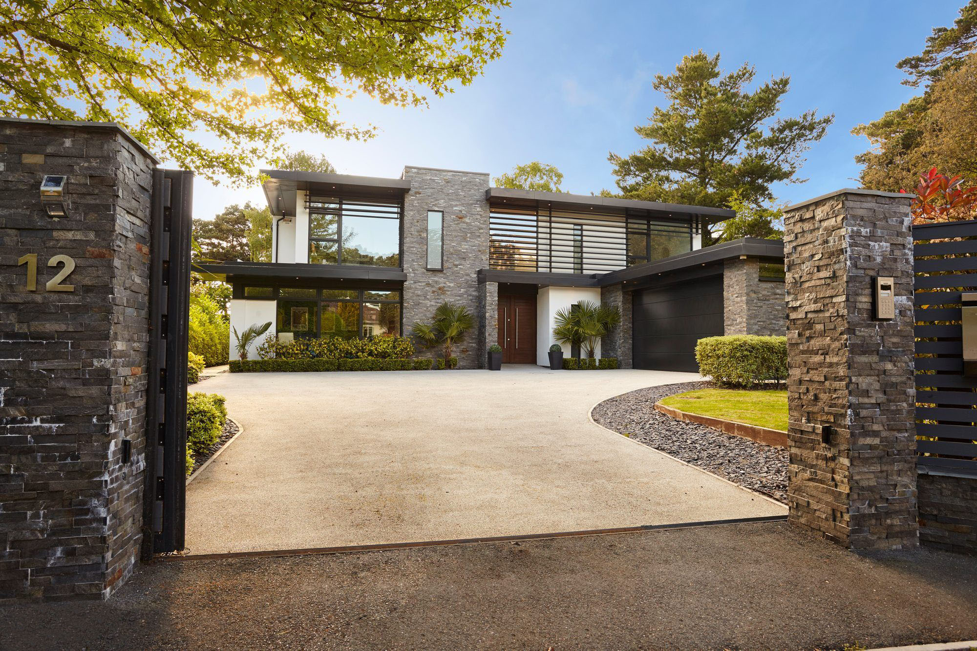 Beautiful modern home design with real stone siding, white stucco and black metal. A real wood front door, black garage door and flat roof complete the exterior design.