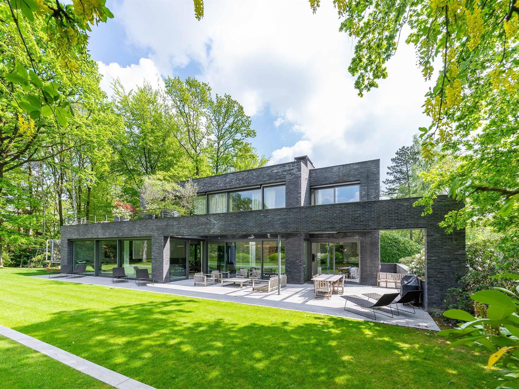 Modern home design featuring dark gray and black brick siding, floor to ceiling windows and a flat roof.