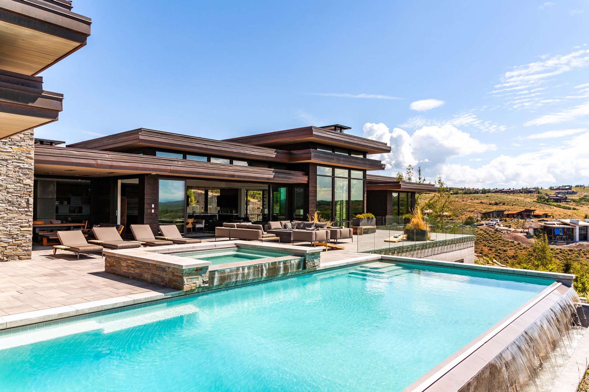 Modern home with wood, metal and stone siding, floor to ceiling windows and an infinity edge pool.