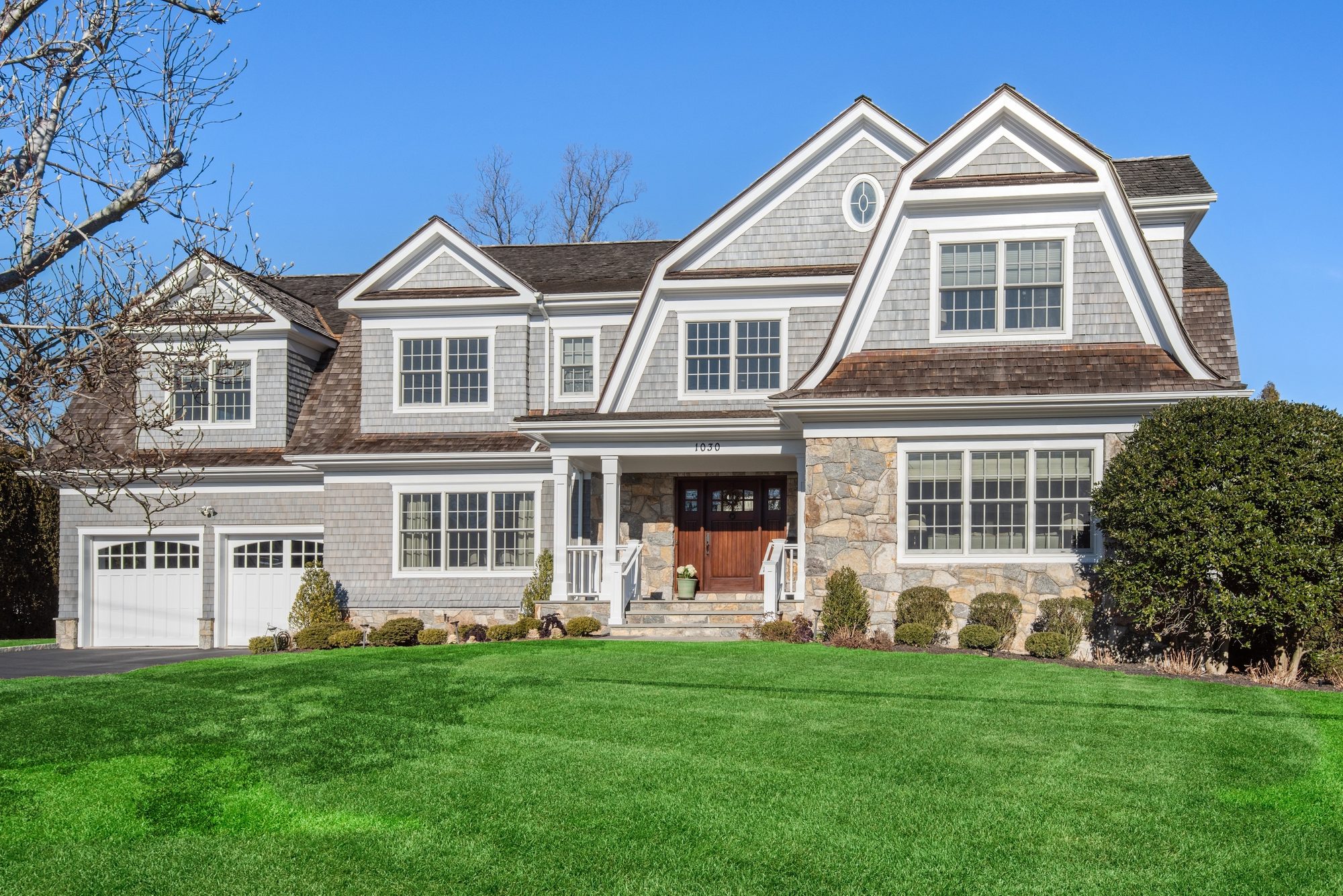 Stunning custom built home with pale gray blue siding and a real wood front door. White garage doors with lots of white trim. Real stone veneer.