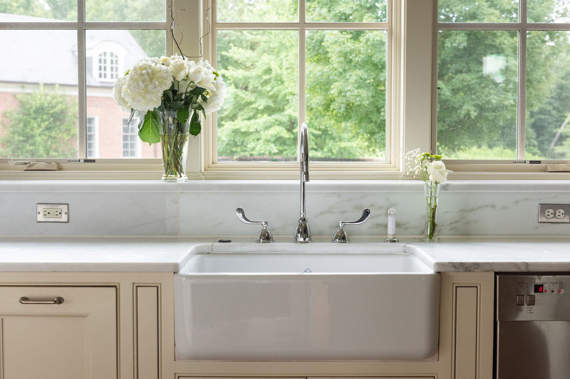 White enamel farmhouse under mount sink with cream cabinets, marble countertops and backsplash.