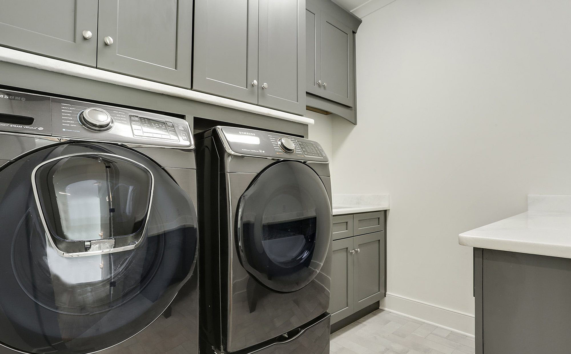 Gray laundry room cabinets, washer and dryer with white marble countertops.