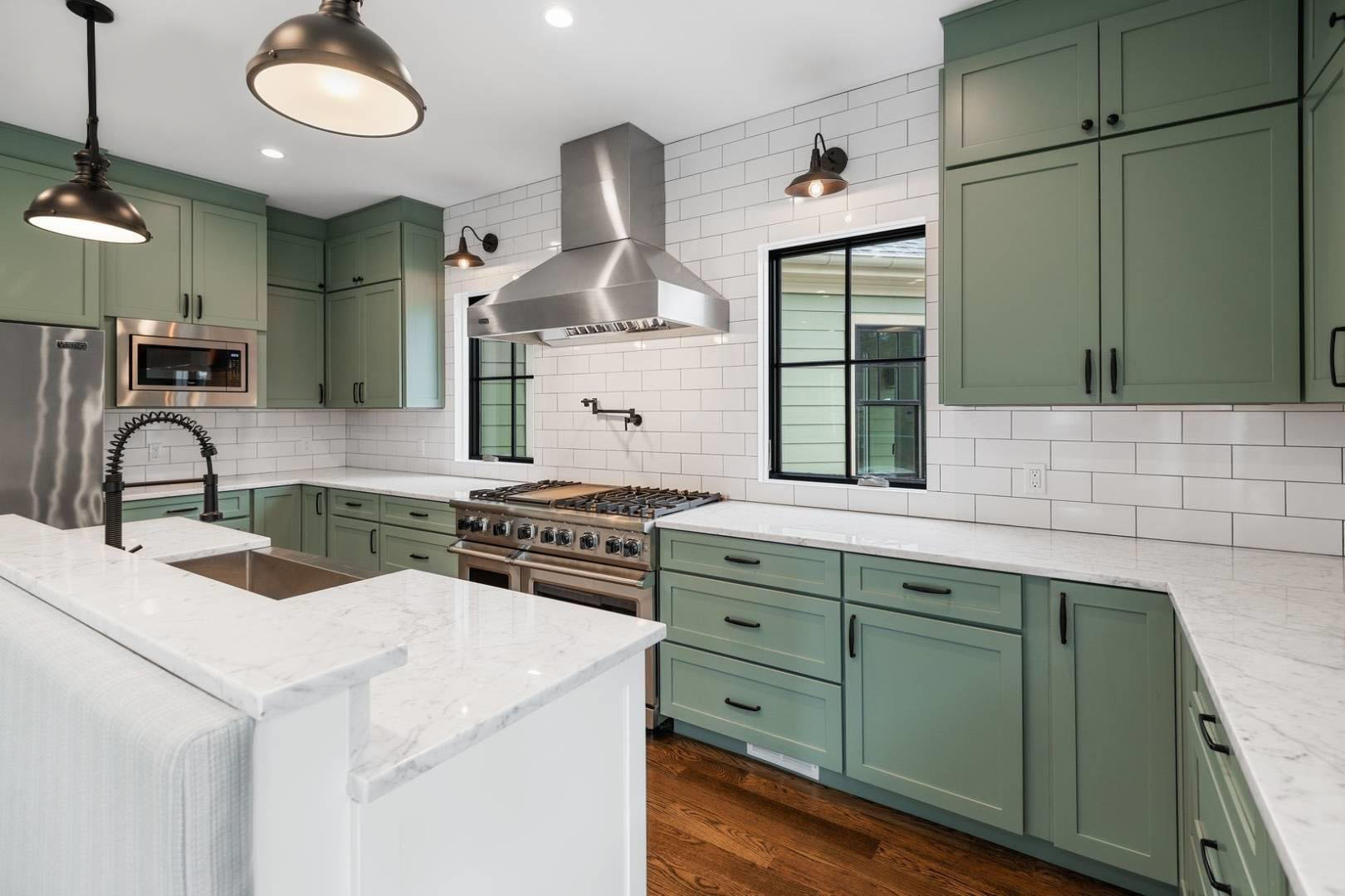 Two tone kitchen cabinets featuring green uppers and lowers with a white island.Black hardware, marble counters and a white subway tile backsplash.