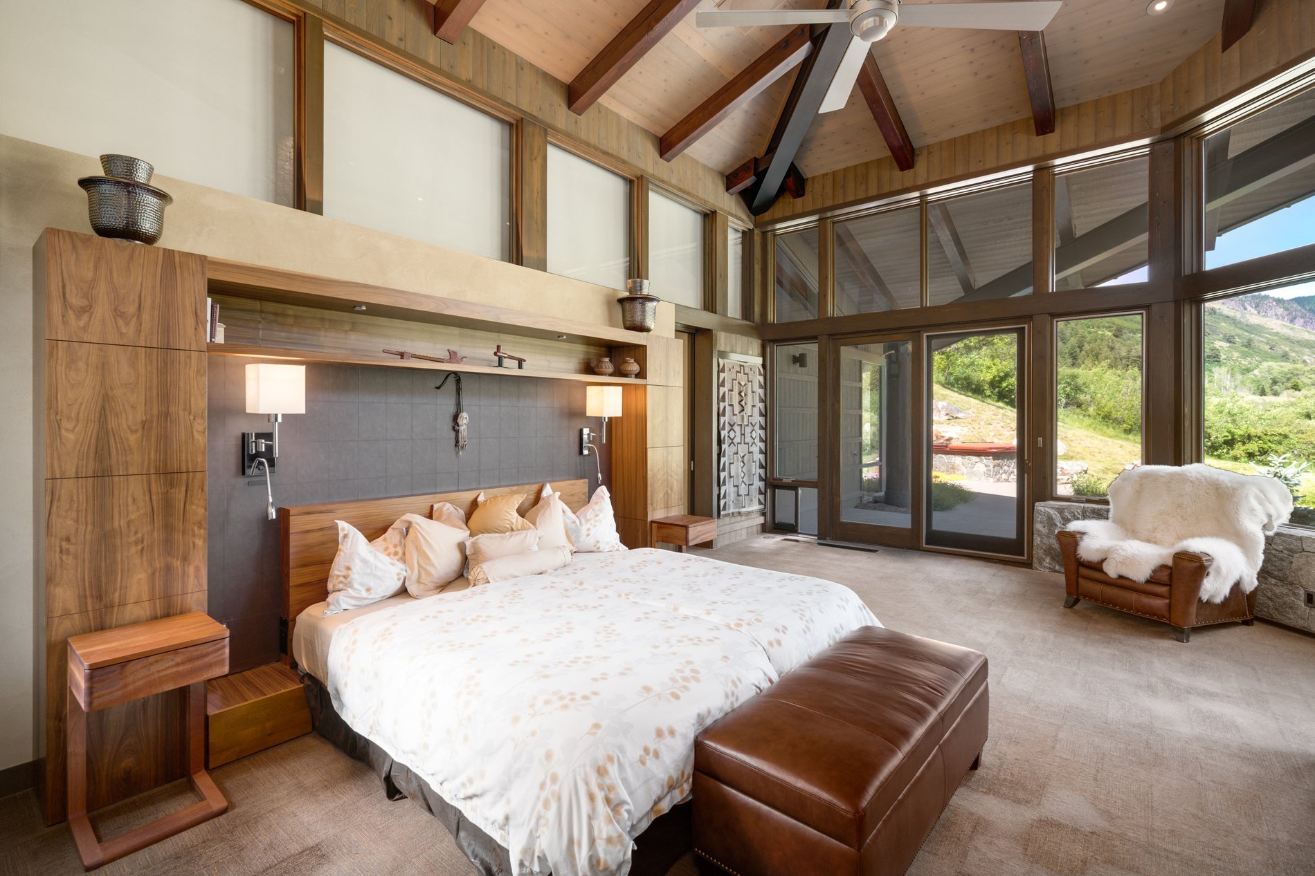 Master bedroom with floor to ceiling glass walls, exposed timber beams and a wood ceiling.