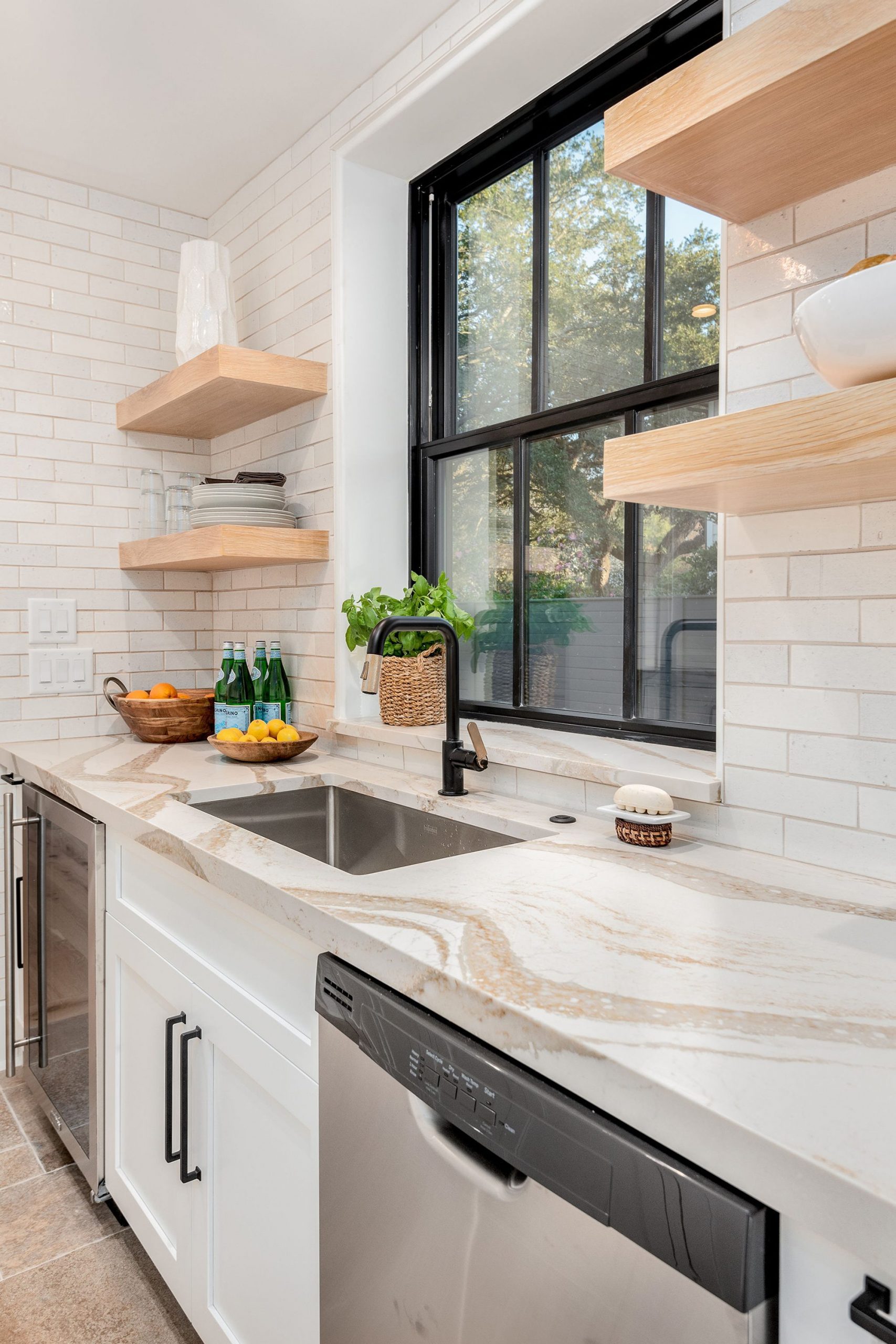beautiful Modern kitchen with white subway tile backsplash, quartz counters & black frame window. light wood shelves. 