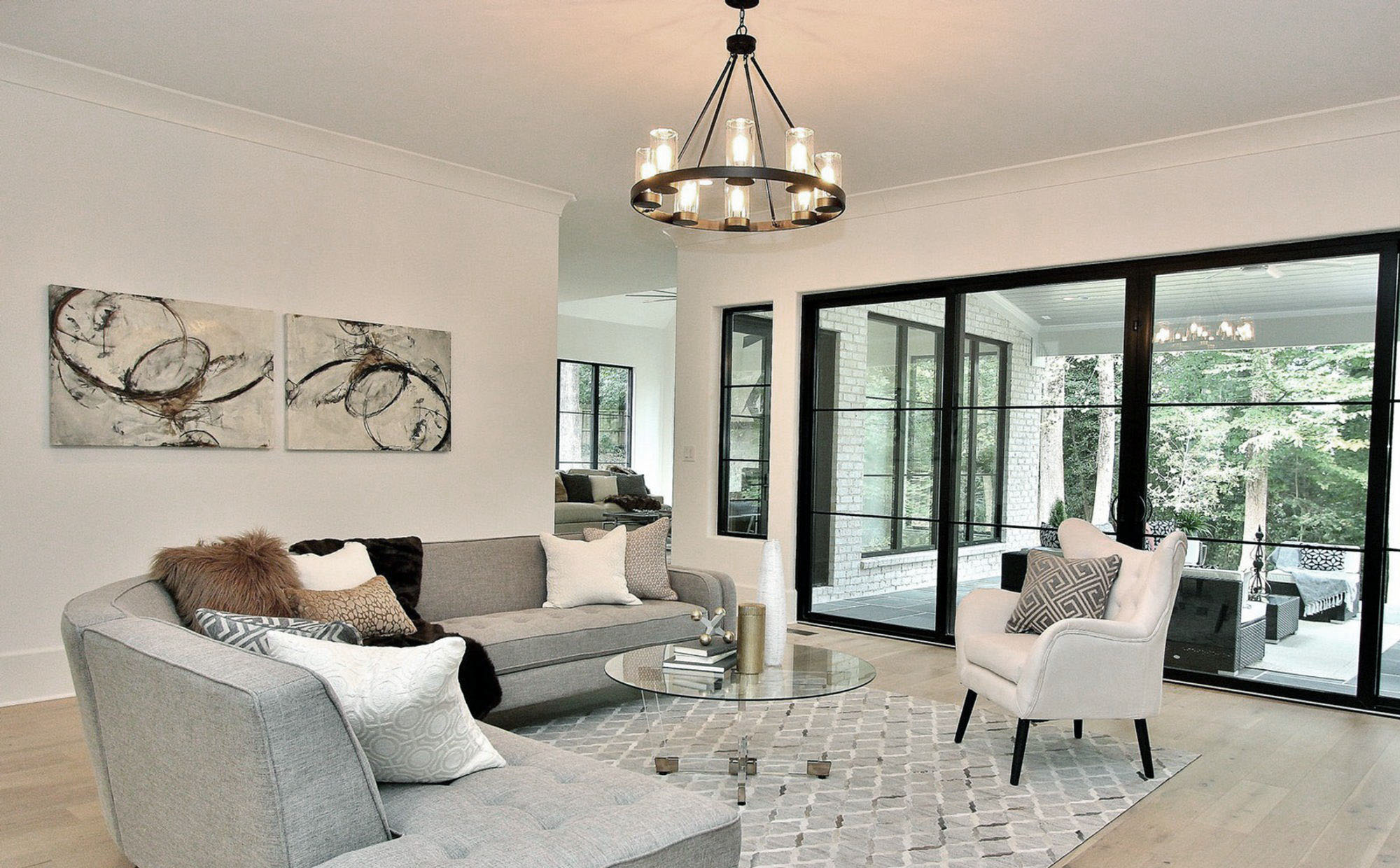 Modern living room with pale grey couch and pattern rug, black frame windows and doors and a pale wood floor.
