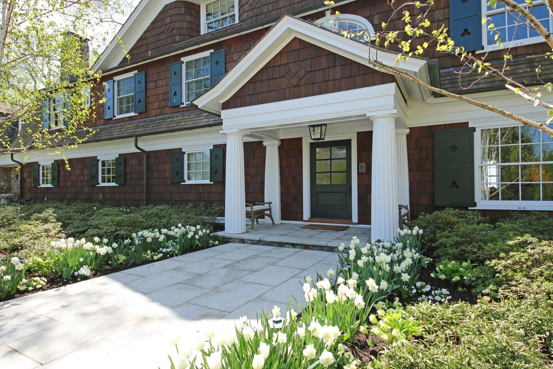 Shingle style a-frame portico with 4 round tapered and fluted columns.