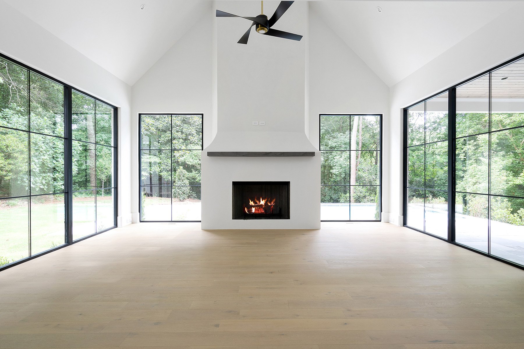 modern living room with a gas fireplace, vaulted ceilings, thin black frame windows, black ceiling fan. 