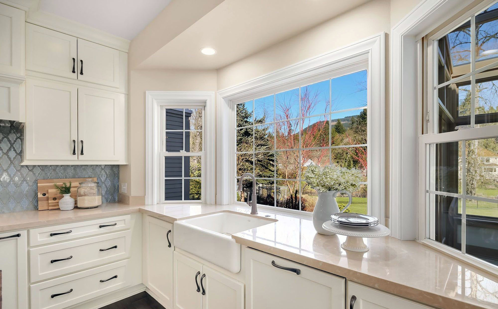 Painted white kitchen cabinets with black hardware, tan stone countertops & a white enamel farm house sink.