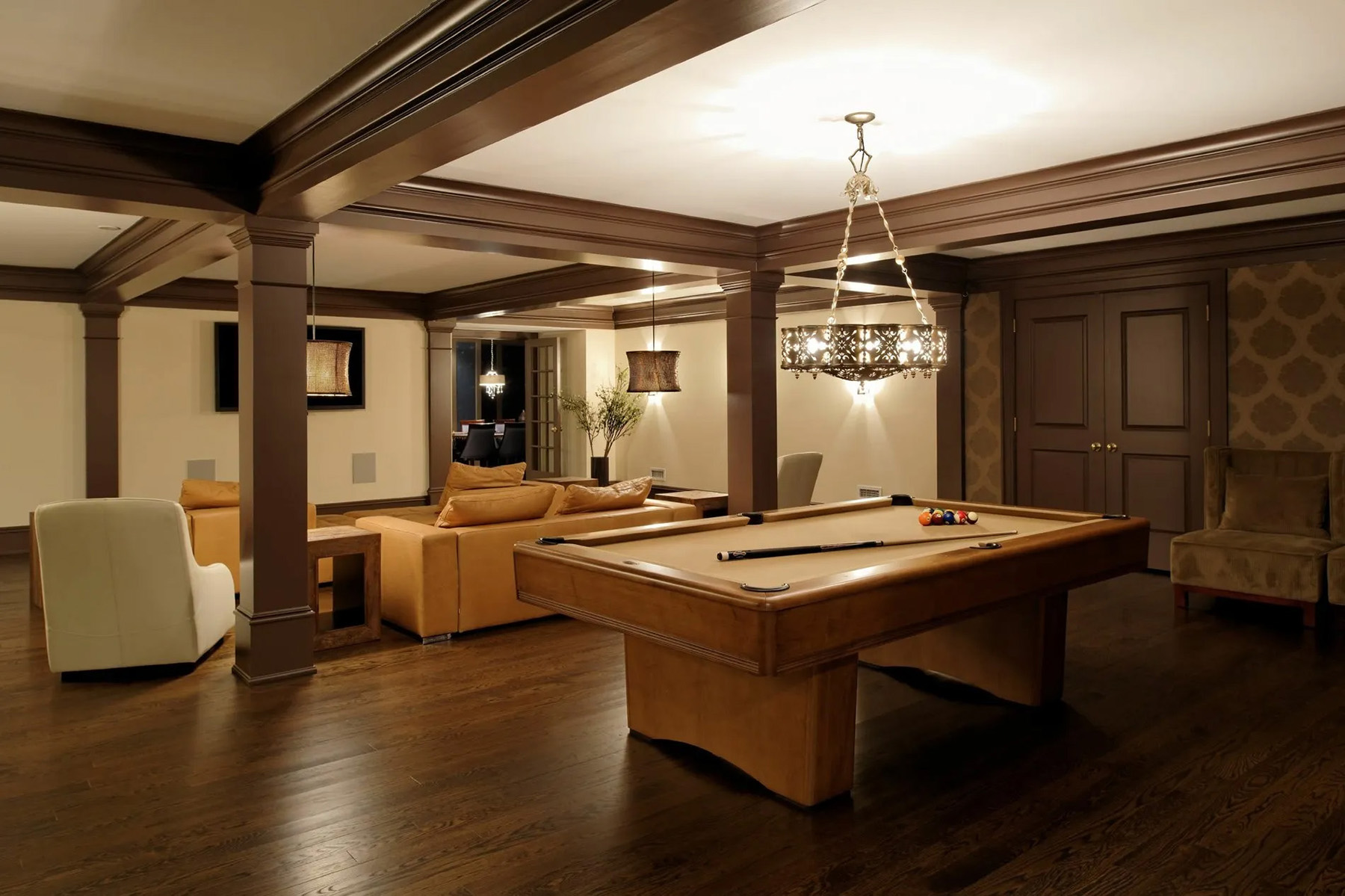 Wood pool table with tan felt. Wood floors with columns and ceiling beams.