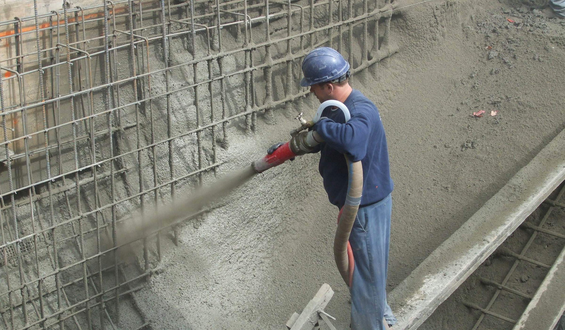 worker shooting gunite concrete onto rebar to build a concrete pool