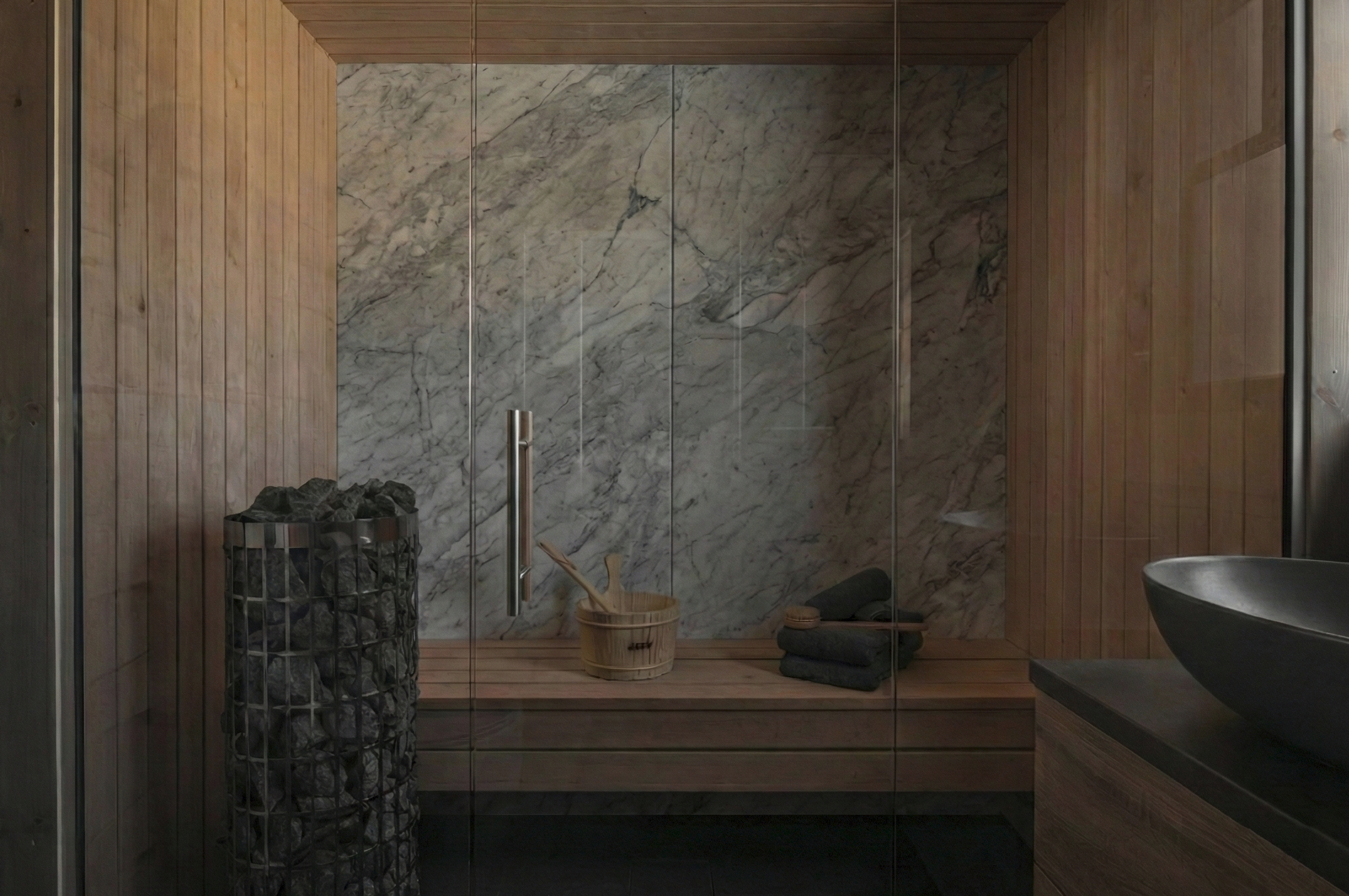 Luxury custom built-in bathroom sauna featuring a solid marble slab back wall, floor-to-ceiling glass front, and stone heater designed by Gambrick Construction in Point Pleasant, NJ.